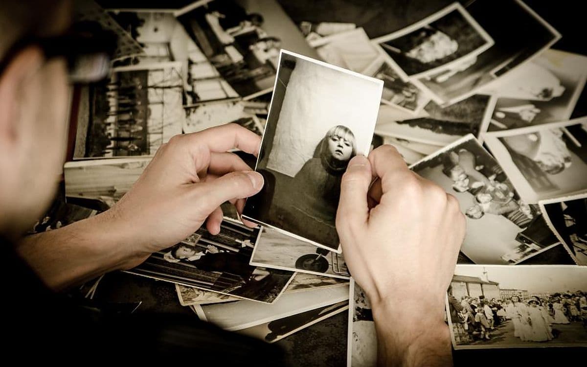 Hands sorting through a big pile of old black-and-white photographs.