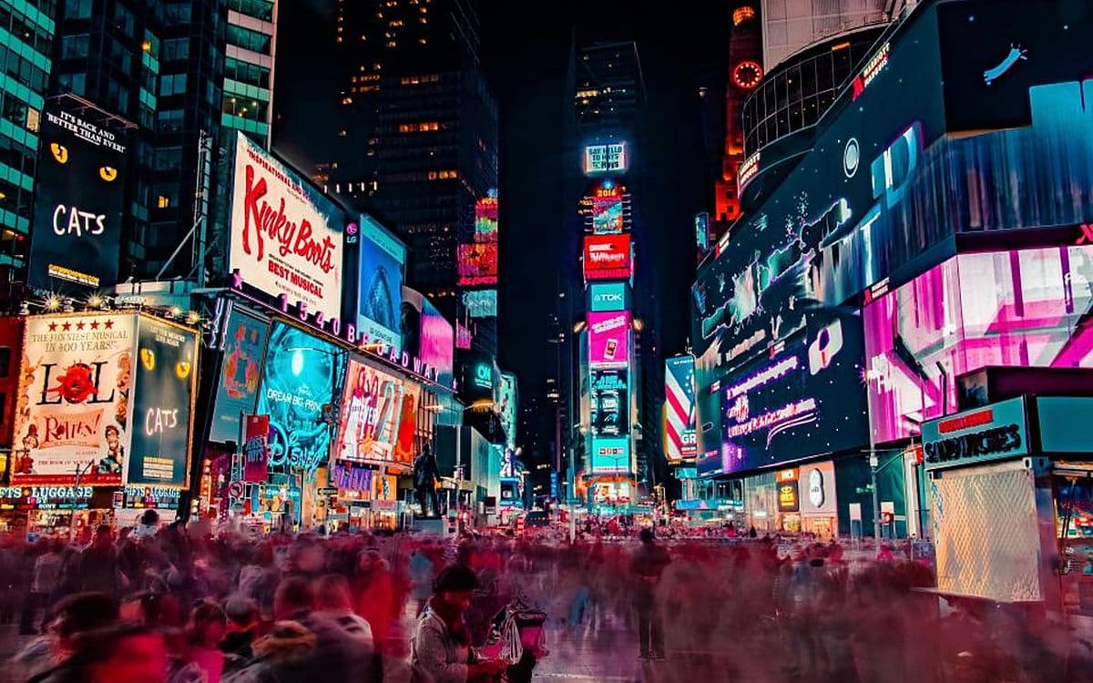 A crowded Times Square at night, neon billboards above a blur of people.