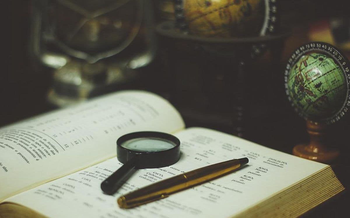 A magnifying glass and a fountain pen resting on an open old book, a globe behind them.