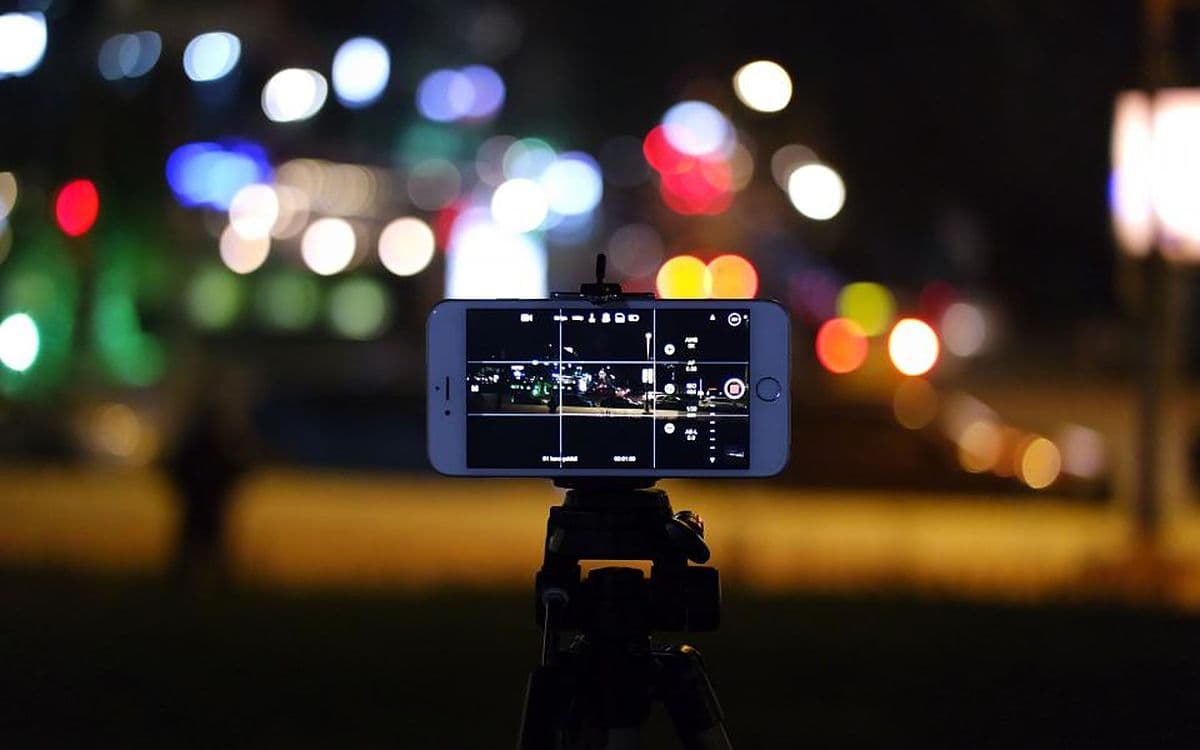 A phone on a small tripod filming a city street at night, lights blurred behind it.