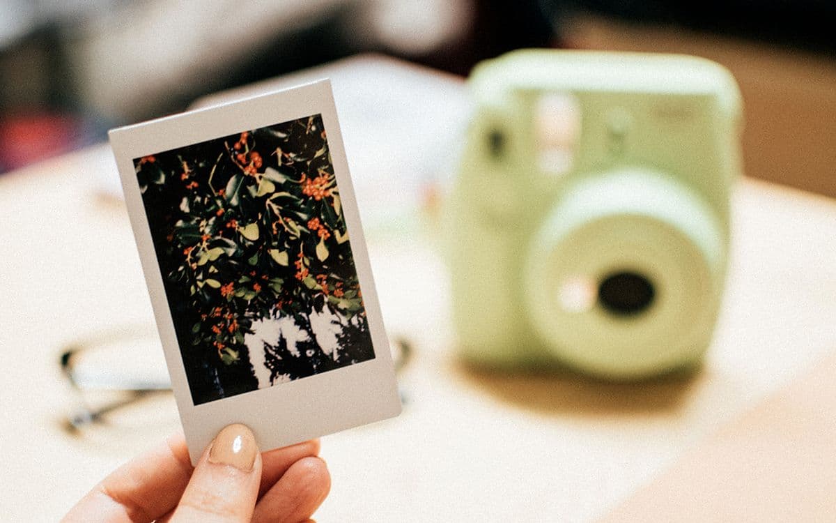 A hand holding up a fresh instant photo, the camera blurred behind it.